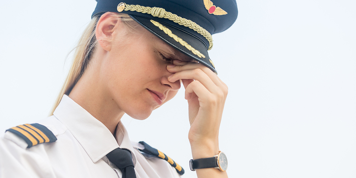 Female aviator in uniform with head down feeling tired and stressed.