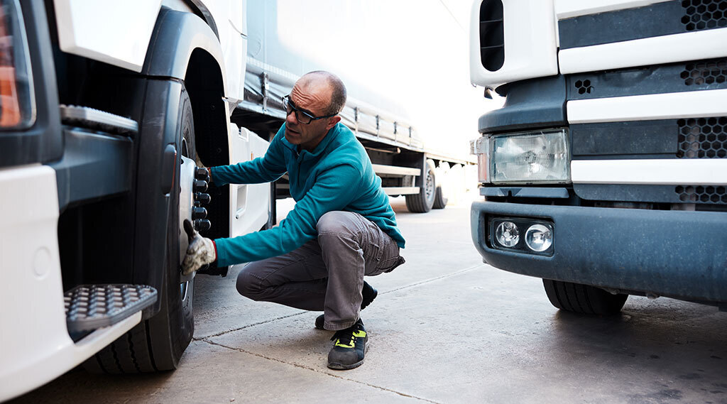 truck driver is squatting next to tractor wheel to examine it for safety