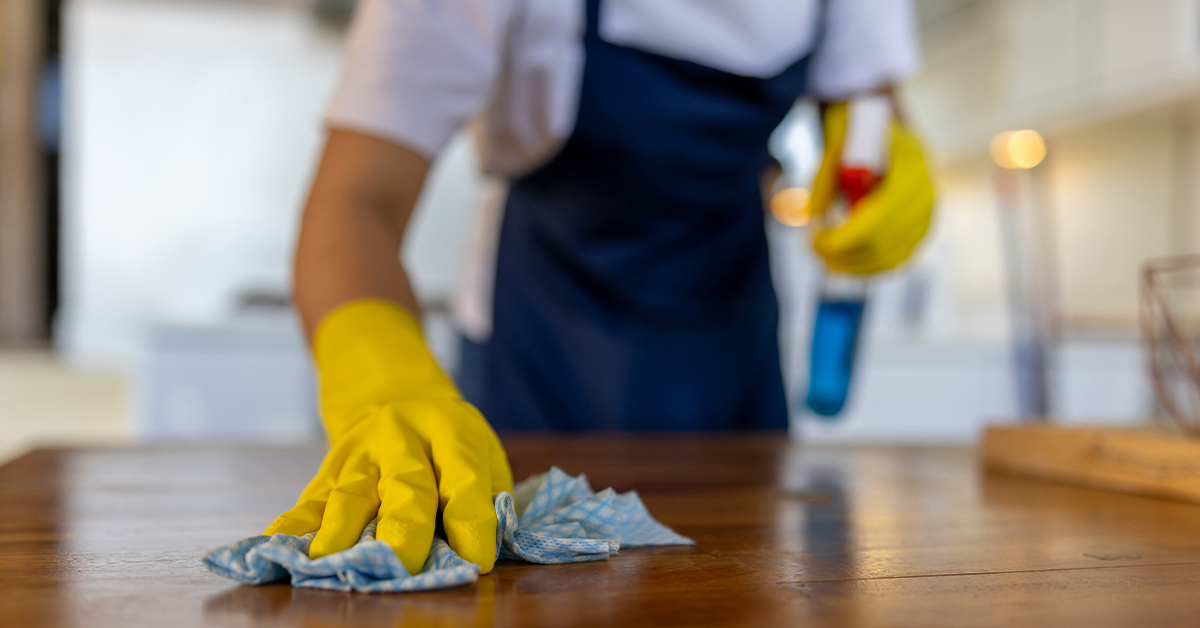 Person with rubber gloves cleaning table with cloth