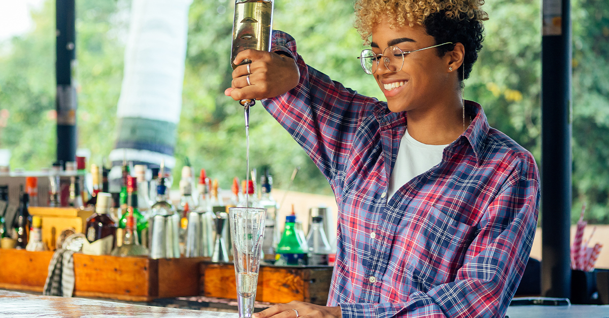 bartender pouring alcohol into glass in sunny outdoor bar area