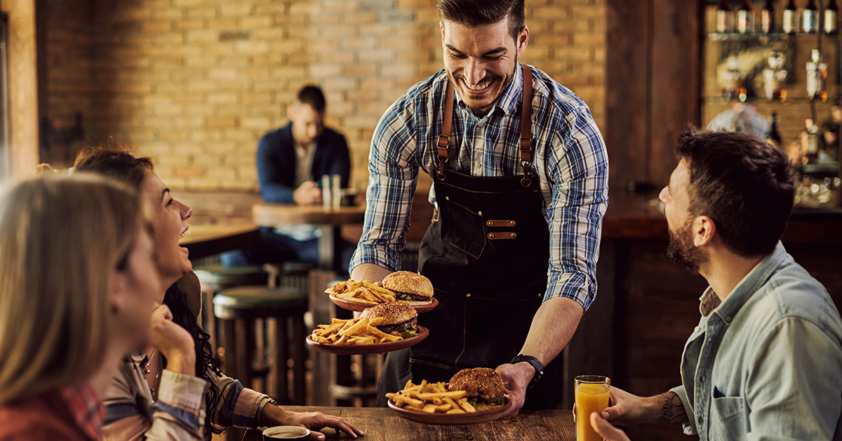 Smiling waiter serving restaurant guests plates of burgers and fries