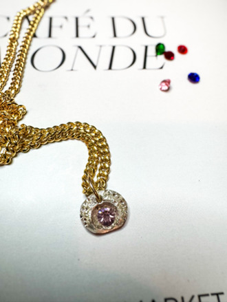 Gold-filled Cuban chain necklace with a sterling silver charm featuring a pink gemstone, displayed on a white background with colorful gemstones scattered nearby