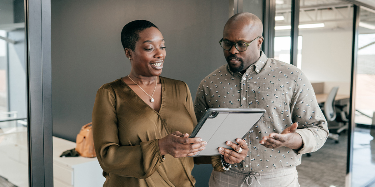 Two office workers examine a handheld tablet