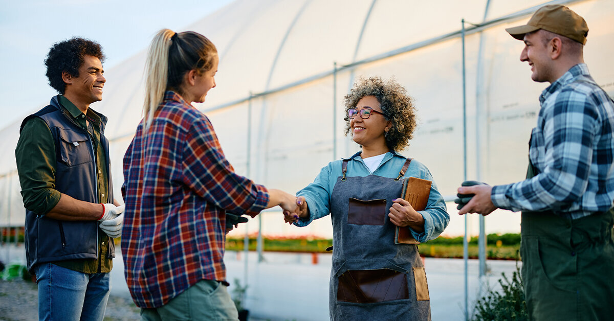 Agricultural workers shake hands in front of a greenhouse