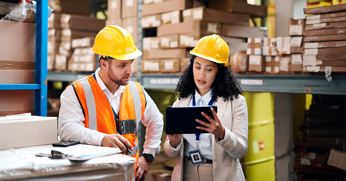 Two people in hard hats look at a clipboard