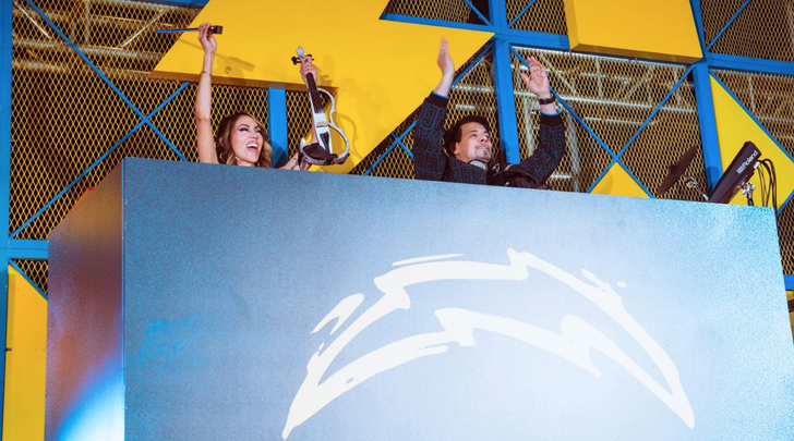 Esther Anaya and Thomas Gold behind a podium featuring the LA Chargers logo at SoFi Stadium